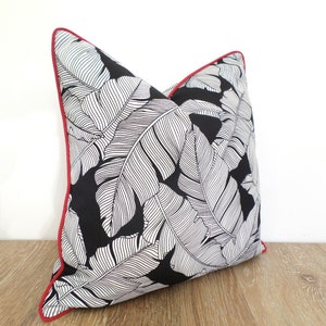 May include: A decorative throw pillow featuring a black background with a white leaf pattern. The pillow has a red trim, adding a pop of color to the design. This accent pillow is a stylish addition to any home decor.