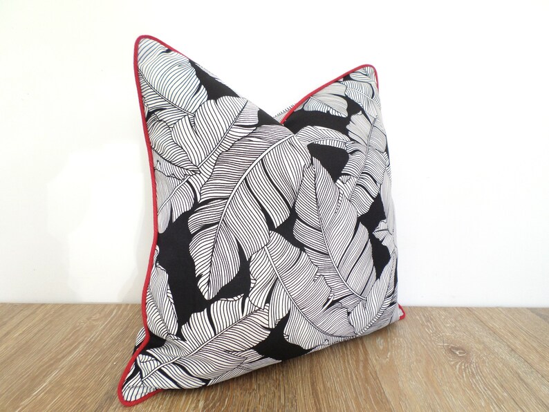 May include: A decorative throw pillow featuring a black background with a white leaf pattern. The pillow has a red trim, adding a pop of color to the design. This accent pillow is a stylish addition to any home decor.