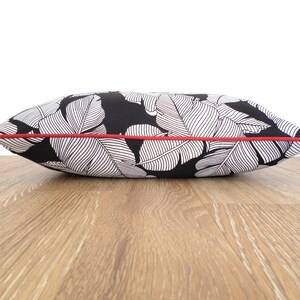 May include: A decorative pillow with a black background and a white leaf pattern. The pillow has a red trim around the edges. The pillow is rectangular and appears to be made of fabric.