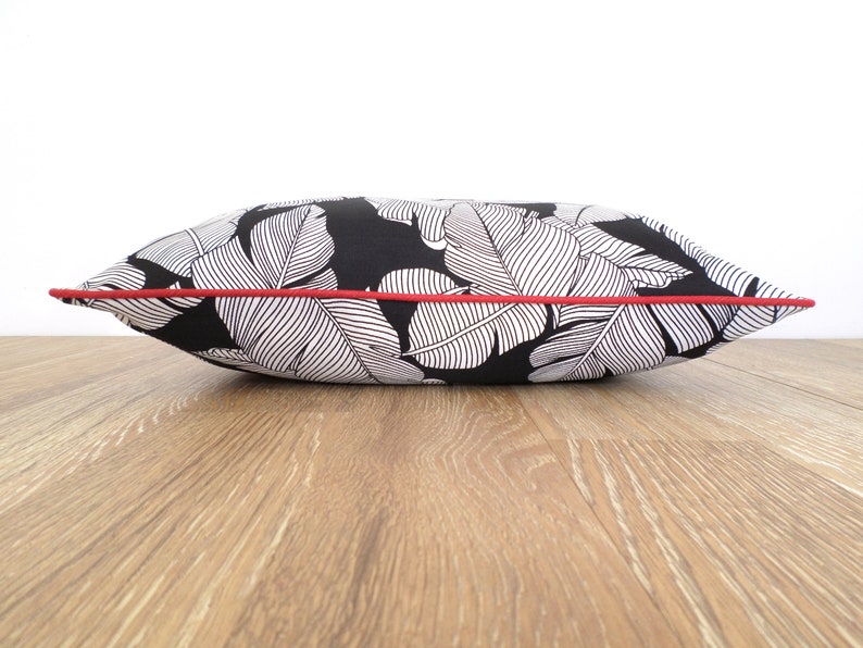 May include: A decorative pillow with a black background and a white leaf pattern. The pillow has a red trim around the edges. The pillow is rectangular and appears to be made of fabric.