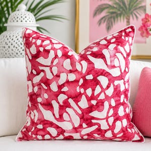 May include: A square throw pillow featuring a vibrant magenta and white abstract pattern that resembles organic, fluid shapes. The pillow is finished with a crisp white piped edge, providing a clean outline to the bold, saturated color design.