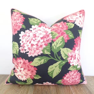 May include: Square decorative pillow with a dark navy background and a floral pattern of pink and white hydrangeas and green leaves. The pillow has a pink trim.