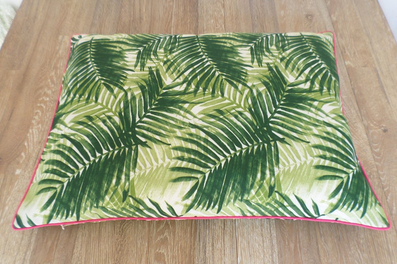 Op de afbeelding: Rechthoekig kussen met een groen palmbladpatroon op een witte achtergrond. Het heeft een felroze rand. Het kussen is waarschijnlijk voor de woondecoratie, afmetingen van ongeveer 40 cm x 60 cm.
