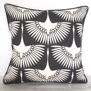 May include: Square throw pillow with a black background and a repeating pattern of white crane illustrations. The pillow has a dark blue border.