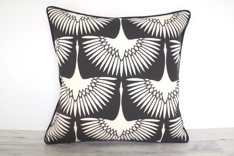 May include: Square throw pillow with a black background and a repeating pattern of white crane illustrations. The pillow has a dark blue border.