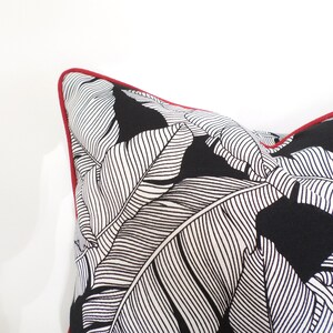 May include: A decorative pillow with a black and white leaf pattern. The pillow has a red trim around the edges. The pillow is a square shape and is made of a soft fabric.