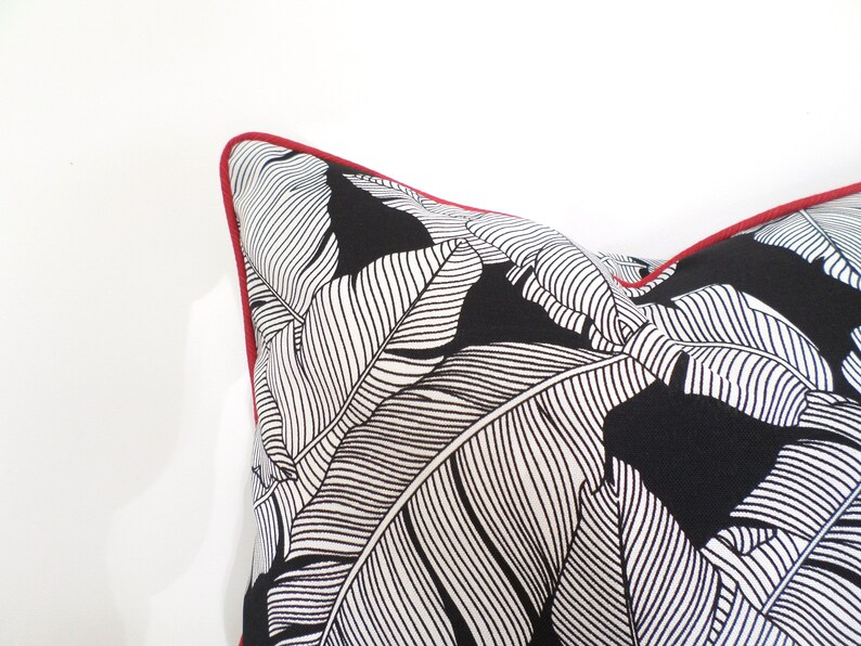 May include: A decorative pillow with a black and white leaf pattern. The pillow has a red trim around the edges. The pillow is a square shape and is made of a soft fabric.