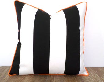 Op de afbeelding: Vierkant decoratief kussen met een opvallend zwart-wit gestreept patroon. Het kussen heeft een helder oranje bies, wat een vleugje kleur aan het ontwerp toevoegt. Geschikt voor interieurdecoratie.
