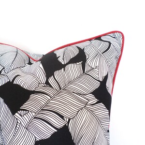 May include: Close-up of a decorative pillow with a black background and white leaf pattern. The pillow has a red trim around the edges. The pillow is a decorative item for a home.