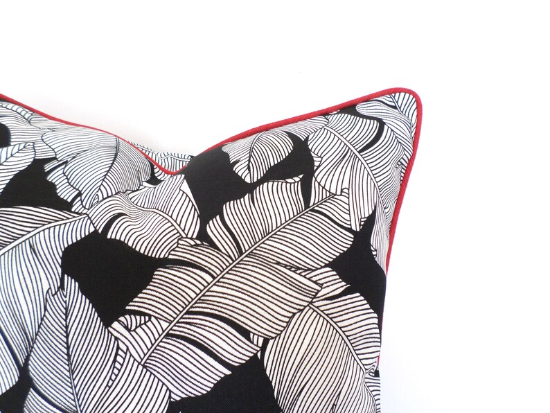 May include: Close-up of a decorative pillow with a black background and white leaf pattern. The pillow has a red trim around the edges. The pillow is a decorative item for a home.
