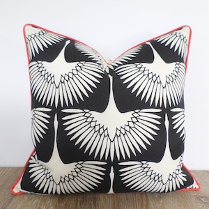 May include: Square decorative pillow with a black background and a repeating pattern of white crane silhouettes. The pillow has a red border, adding a pop of color to the design. The pillow is likely used for home decor.