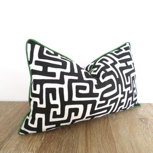 May include: Rectangular decorative pillow with a black and white maze-like pattern. The pillow has a green trim and is placed on a wooden surface. The pillow is designed for home decor.