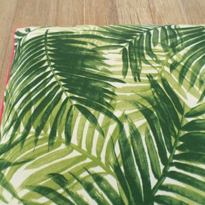 Op de afbeelding: Een rechthoekig kussen met een groen palmbladpatroon op een witte achtergrond. Het heeft een helder roze rand. Het ontwerp roept een tropisch thema op.