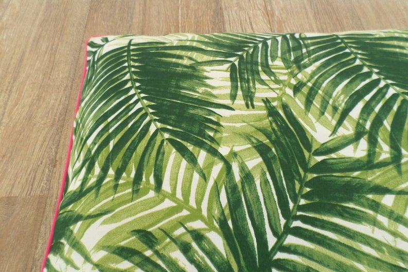 Op de afbeelding: Een rechthoekig kussen met een groen palmbladpatroon op een witte achtergrond. Het heeft een helder roze rand. Het ontwerp roept een tropisch thema op.
