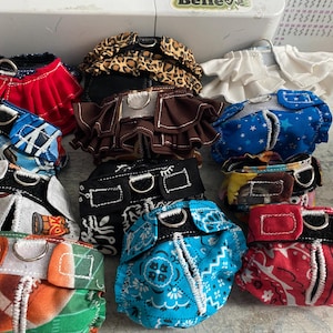 以下が含まれることがあります： 赤、青、茶色など、さまざまな模様のカラフルなペット用おむつのコレクション。デザインには、星、ペイズリー、アニマルプリントなどがあります。各おむつには金属リングと調節可能なストラップが付いています。