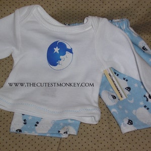 May include: White long-sleeved shirt with a blue crescent moon and star design. The shirt is paired with blue and white pyjama pants featuring a sheep pattern and the text "The Cutest Monkey Look".