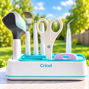 May include: A white and teal Cricut tool organizer base holding a collection of crafting implements, including a brayer, spatula, weeding tools, scissors, and a scraper. The organizer features a white body with a teal accent stripe and the Cricut logo.