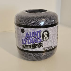 May include: Aunt Lydia's Classic Crochet thread in a dark gray color, wrapped in clear plastic. The label features the brand name, a woman's silhouette, and the words "Classic Crochet". The thread is 100% mercerized cotton.