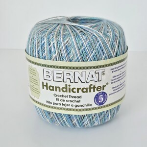 May include: A ball of Bernat Handicrafter crochet thread in shades of blue, white, and gray. The label indicates it is size 5. The thread is ideal for garments, accessories, and home decorating projects.