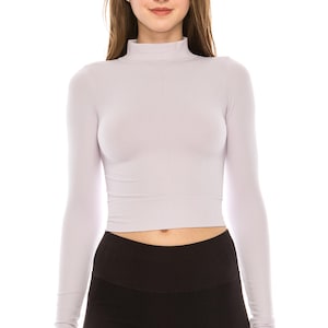 May include: A light purple, long-sleeved crop top with a mock neck. The top is paired with black leggings. The model is centered in front of a white background.