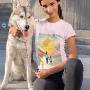Puede incluir: Una mujer con una camiseta rosa con un gráfico de una puesta de sol y el texto "Proud Autism Mum" está sentada en una escalera de hormigón con un perro husky.
