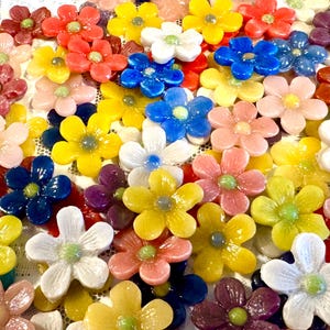 May include: A collection of small, five-petaled glass flowers in a variety of vibrant colors including yellow, blue, pink, white, red, and purple. Each flower features a smooth, glossy finish and a small, round center dot in a contrasting color.