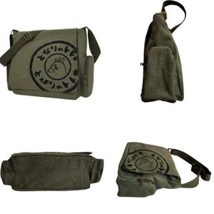May include: Olive green canvas messenger bag with a flap closure, adjustable shoulder strap, and a small side pocket. The bag features a black circular graphic with Japanese text and a cartoon character.