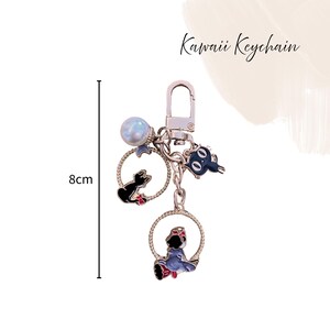 Pu&ograve; includere: Un portachiavi argentato con tre ciondoli. I ciondoli includono un gatto nero, un personaggio blu e rosso e un gatto nero con un fiocco blu. Il portachiavi &egrave; lungo 8 cm e presenta la scritta "Kawaii Keychain".