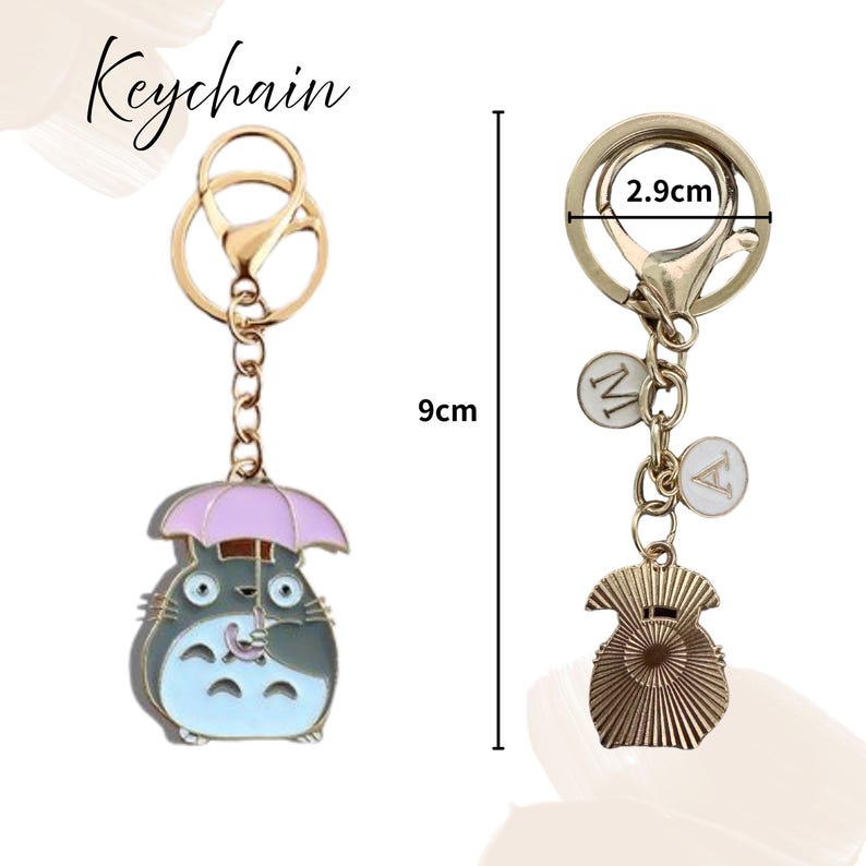 May include: A gold-colored keychain with a cartoon character holding an umbrella, measuring 9cm in length. The keychain also features a charm with the letter "A" and a decorative element. The clasp is 2.9cm wide.