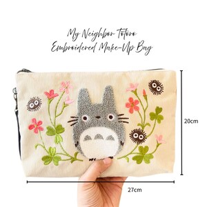 May include: Cream corduroy makeup bag with an embroidered Totoro design. The bag has a zip closure and is 27 cm long and 20 cm high. The design includes pink flowers and green leaves.