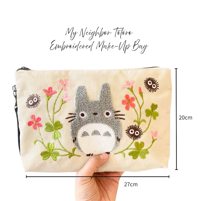 May include: Cream corduroy makeup bag with an embroidered Totoro design. The bag has a zip closure and is 27 cm long and 20 cm high. The design includes pink flowers and green leaves.