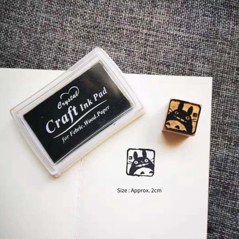 May include: A black ink pad labelled "Crystal Craft Ink Pad for Fabric, Wood, Paper" with a clear plastic case. Next to it is a small wooden stamp with a black and white illustration of a cartoon character with large ears.