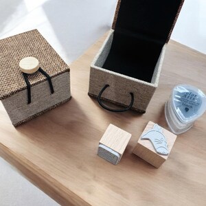 May include: A set of wooden stamps featuring a cat design, a small box with a fabric cover, and a black ink pad. The ink pad has the text "Color Arts" and "black" on it.