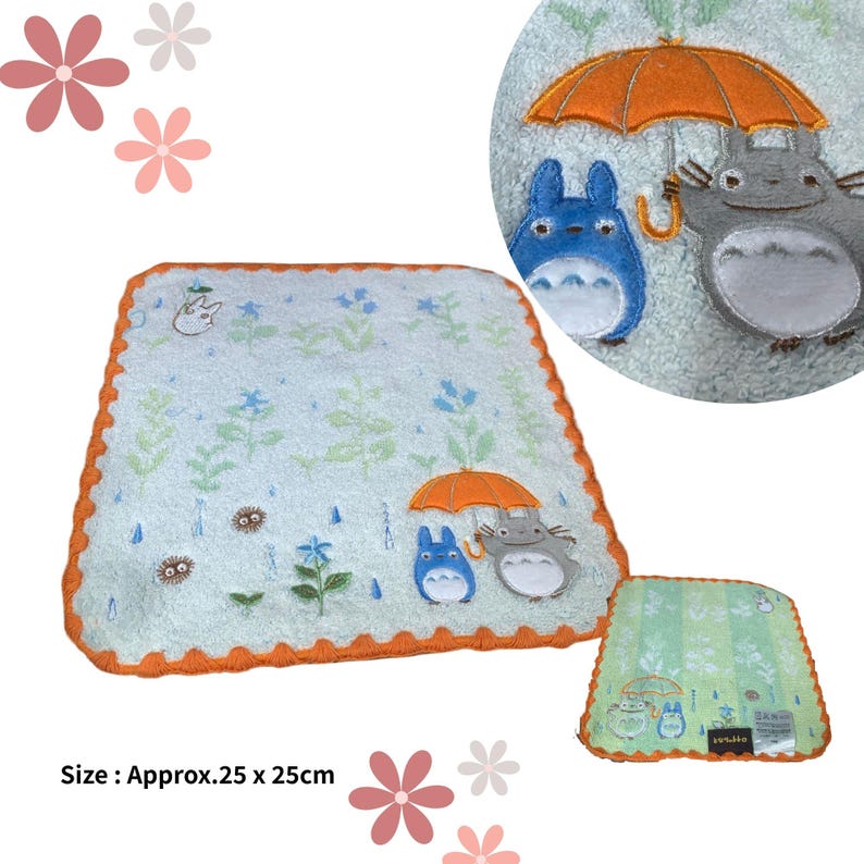 May include: A light blue, approximately 9.8 x 9.8 inch, square towel with an orange scalloped border. The towel features embroidered images of Totoro characters under an orange umbrella, with floral and rain drop details.
