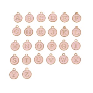 May include: A collection of gold-colored alphabet charms, each with a light pink enamel background. The charms are round with a loop at the top for attaching to jewelry. The letters A through Z are displayed.