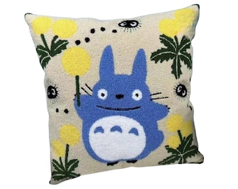 May include: Square decorative pillow featuring a blue cartoon character holding a yellow flower. The pillow has a beige background with yellow flowers, green leaves, and black eye designs. The pillow has a white border.