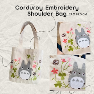May include: Cream-colored corduroy shoulder bag with embroidered design. The bag features a gray cartoon character with floral and clover accents. The bag measures 24 x 28.5 cm.