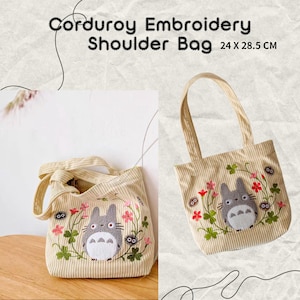 May include: Beige corduroy shoulder bag with an embroidered cartoon character design. The bag features a striped pattern and a tote-style handle. The bag measures 24 x 28.5 cm.