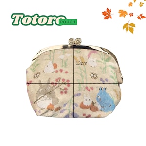 May include: A beige pouch with a metal clasp, featuring a Totoro design with characters and floral elements. The pouch measures 17cm wide and 13cm high. The word "Pouch" is written in green.