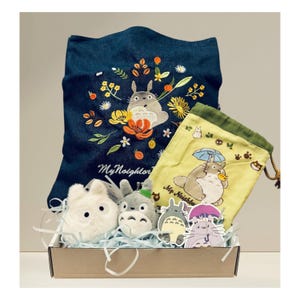 May include: A gift set featuring embroidered denim tote bag, yellow drawstring bag, plush toys, and stickers. The tote bag has a floral and Totoro design with the text "My Neighbor". The drawstring bag has a Totoro design with an umbrella. The set is in a cardboard box.