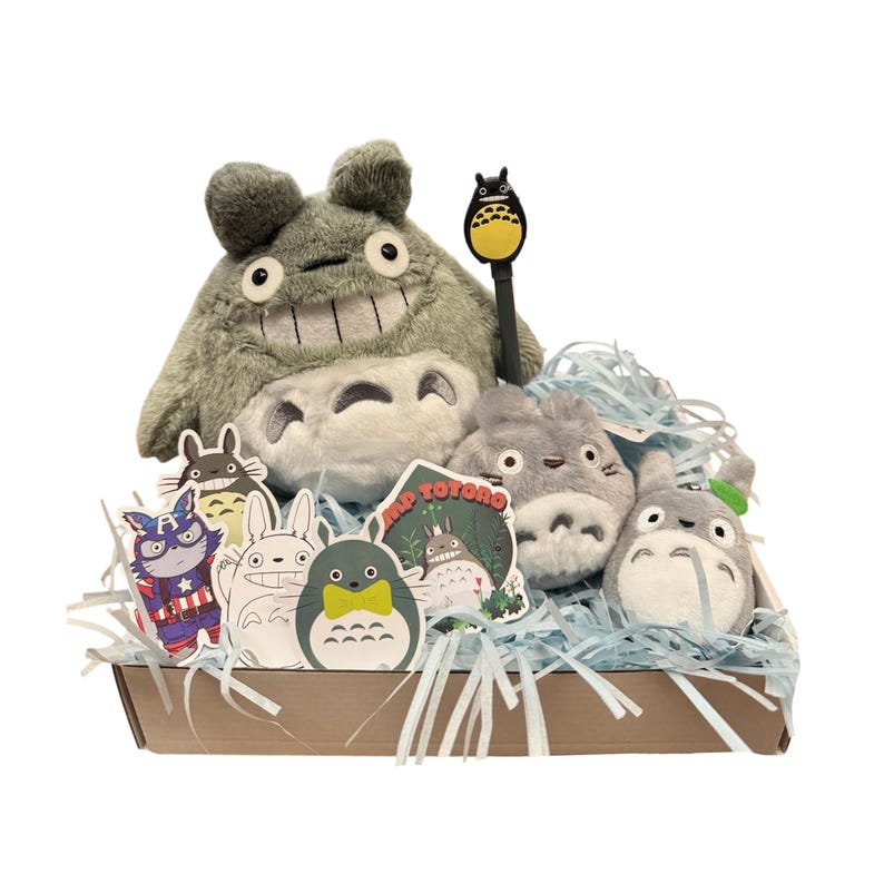 May include: A gift basket filled with Totoro-themed plush toys and stickers. The basket contains a large gray Totoro plush, smaller Totoro plushies, and various character stickers. A pen with a Totoro topper is also included. The basket is lined with blue paper shreds.