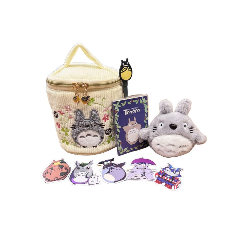 May include: A collection of Studio Ghibli's Totoro-themed merchandise. Includes a cream-colored cosmetic bag with embroidered Totoro, a plush Totoro, stickers, a pen, and a small book titled "Totoro".