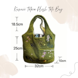 K&ouml;nnte beinhalten: Eine gr&uuml;ne Pl&uuml;sch-Tragetasche mit gestickten Details, darunter Blumen und Bl&auml;tter. Die Tasche, 10 cm tief, 32 cm breit und 25 cm hoch, hat eine Tasche und den Text "Kawaii Totoro Plush Tote Bag".