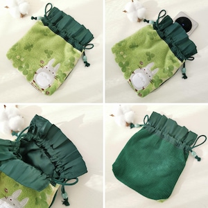 May include: Green drawstring pouch with a cartoon character design. The pouch has a ruffled top and a drawstring closure. The main body is light green with a floral pattern and a cartoon character. The drawstring is dark green.