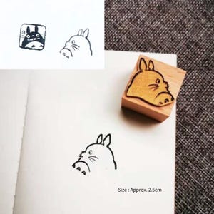 May include: A wooden stamp featuring a cartoon image of Totoro, a character from the animated film My Neighbour Totoro. The stamp measures approximately 2.5 cm in size.