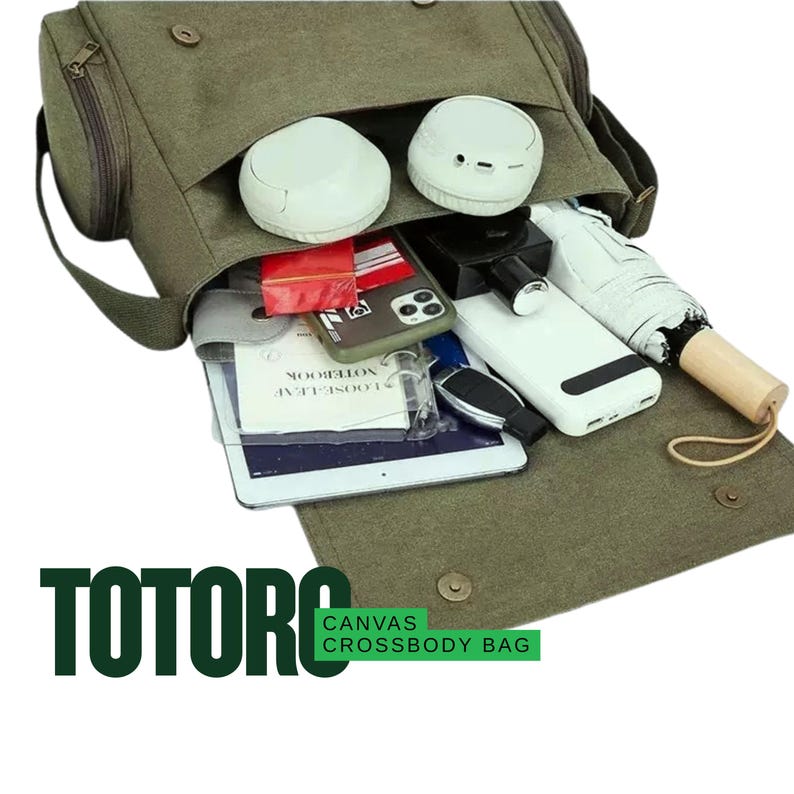 May include: Olive green canvas crossbody bag with a flap closure, open to reveal white earbuds, a smartphone, a tablet, and other personal items. The bag has a shoulder strap and the word "TOTORO" is printed on the front.