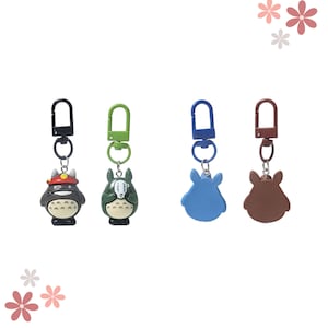 May include: Four keychains with cartoon character designs. The keychains feature a black and red character, a green and white character, a blue character, and a brown character. Each keychain has a metal clasp in a different colour.