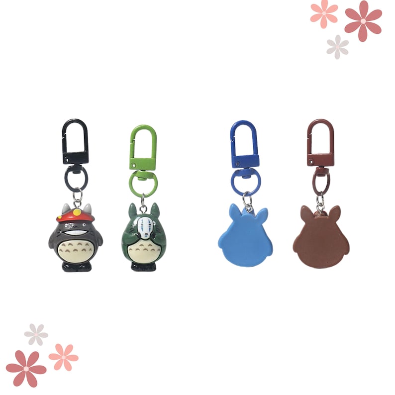 May include: Four keychains with cartoon character designs. The keychains feature a black and red character, a green and white character, a blue character, and a brown character. Each keychain has a metal clasp in a different colour.