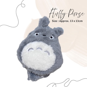 May include: A grey plush purse in the shape of a cartoon character, with a white belly and embroidered facial features. The purse is approximately 13 x 13 cm. The text "Huffy Purse" is written in cursive.