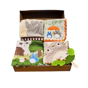 May include: A set of four embroidered washcloths featuring characters from a popular animated film, presented in a brown box. The washcloths showcase various scenes with the characters in different settings, with a variety of colors including beige, green, and blue.